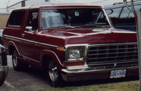 1985 Ford Bronco - A maroon 1980s Ford Bronco is parked outdoors, showing its front three-quarter view. The vehicle features chrome trim and a chrome grille,…