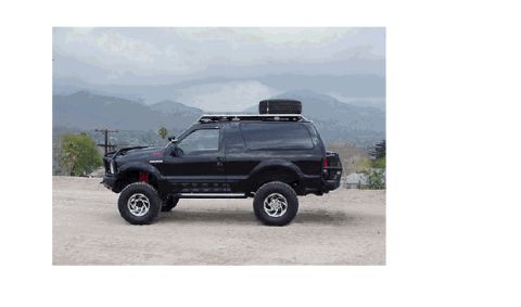 1985 Ford Bronco - A lifted, black, two-door SUV is parked on a dirt lot with mountains in the background. The vehicle has a roof rack with a spare tire and o…