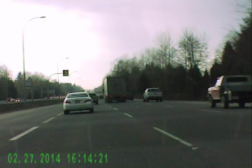 Light sedan and dark pickup truck on a highway, cloudy sky, timestamp.