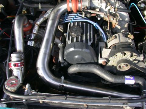 1985 Ford Bronco - A close-up view of a modified engine bay, featuring a turbocharger, intercooler piping, and a blow-off valve.