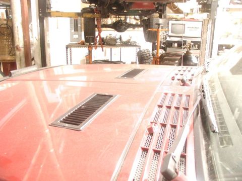 1985 Ford Bronco - A red vehicle's hood is shown with two rectangular vents and a textured panel with multiple small vent openings. A vehicle's undercarriage…