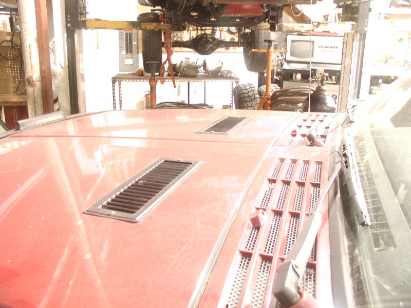 Red vehicle hood with vents, vehicle undercarriage on a lift in background.