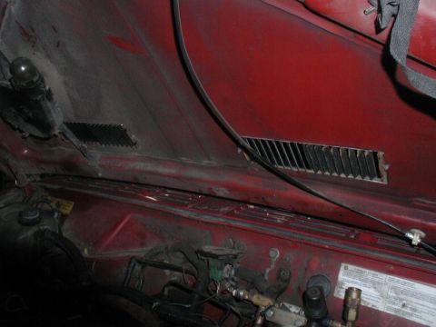 1985 Ford Bronco - The underside of a red vehicle's hood is shown, revealing vents and various engine components and wiring. A black strap is visible attached…