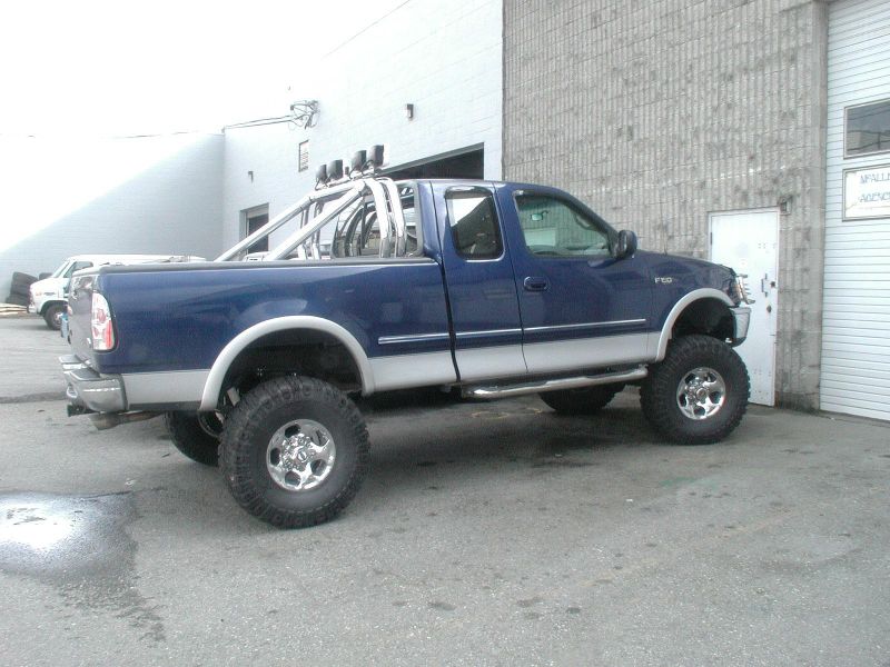 Lifted blue and silver pickup truck with chrome roll bar and lights parked outside.