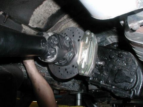 1985 Ford Bronco - A mechanic's hand is visible as they work on the rear differential and driveshaft of a vehicle. A large, drilled brake rotor and caliper ar…