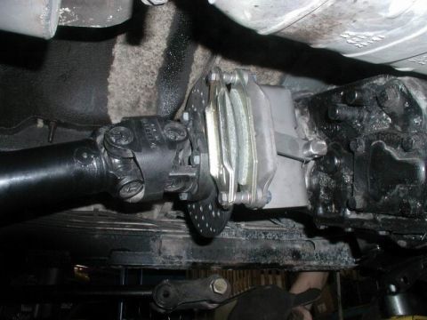 1985 Ford Bronco - The underside of a vehicle shows a driveshaft connected to a differential with a brake rotor and caliper assembly. The components appear to…