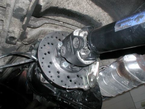 1985 Ford Bronco - Close-up view of a custom rear axle modification on a vehicle, featuring a drilled brake rotor attached to the differential and a driveshaf…