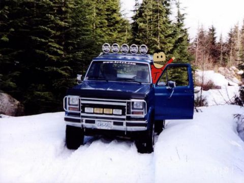 1985 Ford Bronco - A blue Ford Bronco is parked in a snowy forest with its driver's side door open. The vehicle has a light bar on the roof and a bull bar on…