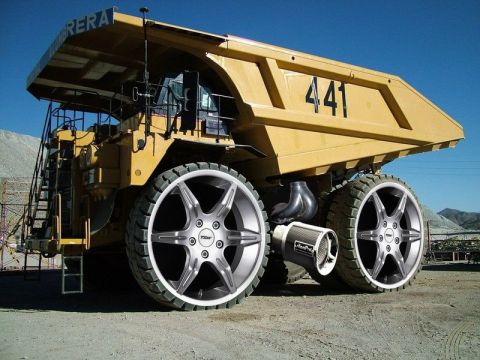 1985 Ford Bronco - A heavily modified yellow mining dump truck is shown with custom large diameter rims and tires, and an aftermarket exhaust system. The truc…