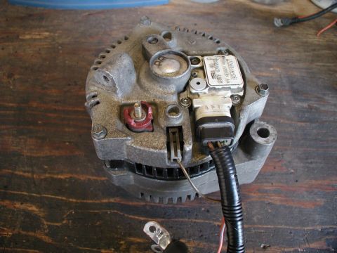 1985 Ford Bronco - A close-up, overhead view of a used alternator, likely from a Ford vehicle, resting on a wooden workbench. The alternator shows some wear a…