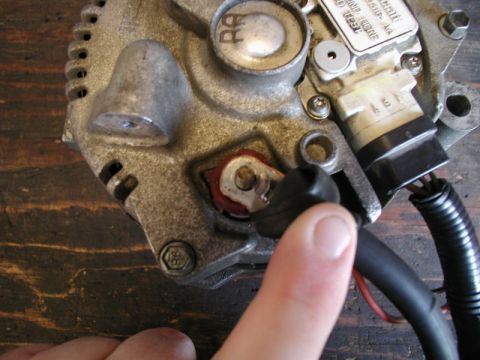 1985 Ford Bronco - A close-up view of an alternator part, with a finger pointing to a black rubber boot covering a terminal. The alternator is mounted on a wo…