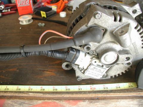 1985 Ford Bronco - A close-up view shows a rebuilt alternator with a wiring harness attached, resting on a wooden surface next to a tape measure. The alternat…