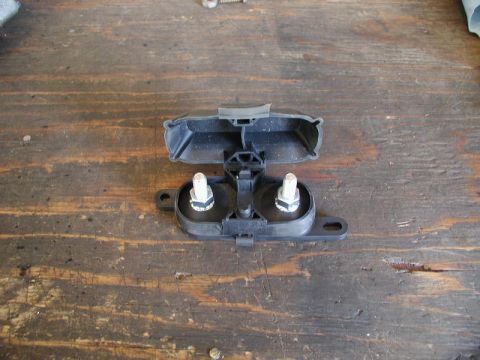 1985 Ford Bronco - A black plastic automotive part with two bolts and nuts is shown resting on a wooden surface. The part appears to be a cover or housing for…