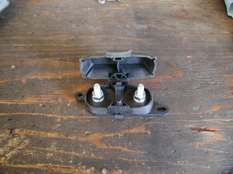 Black plastic automotive part with two bolts on a wooden surface