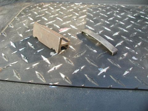 1985 Ford Bronco - Two metal parts are shown on a diamond plate surface. One part is an I-beam shaped metal piece, and the other is a curved metal strip.