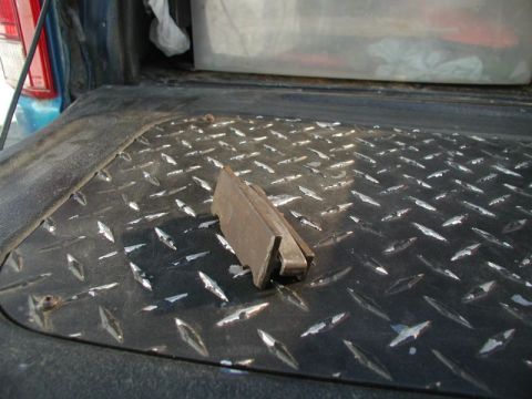 1985 Ford Bronco - A metal bracket rests on the diamond plate bed liner of a pickup truck. The truck's tailgate and taillight are visible in the background.