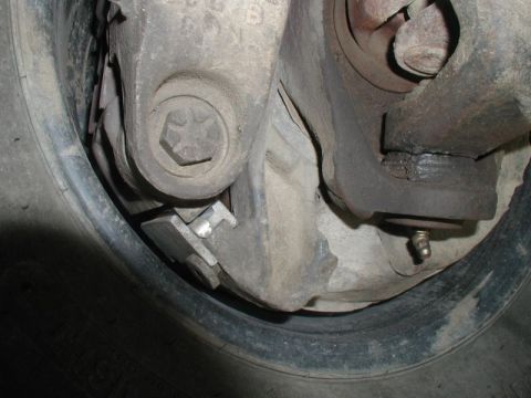 1985 Ford Bronco - A close-up view of the brake assembly of a vehicle, showing brake pads, a caliper bracket, and a wheel hub. A grease fitting is visible on…