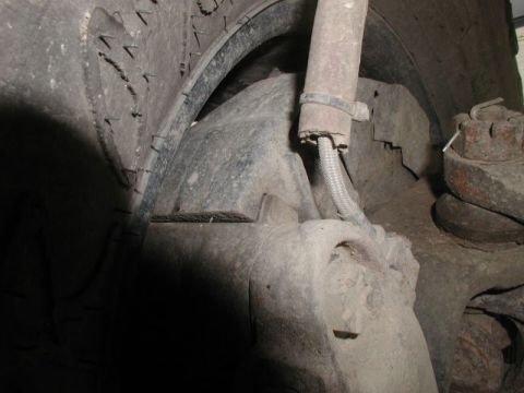 1985 Ford Bronco - A close-up view of the underside of a vehicle, showing a heavily soiled tire, suspension components including a shock absorber, and a large…