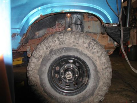 1985 Ford Bronco - A close-up view of the rear wheel well of a blue Ford Bronco, showing significant rust damage to the inner fender and surrounding body pane…
