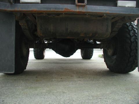 1985 Ford Bronco - The underside of a vehicle, showing the rear differential, leaf springs, fuel tank, and large off-road tires. The vehicle appears to be par…