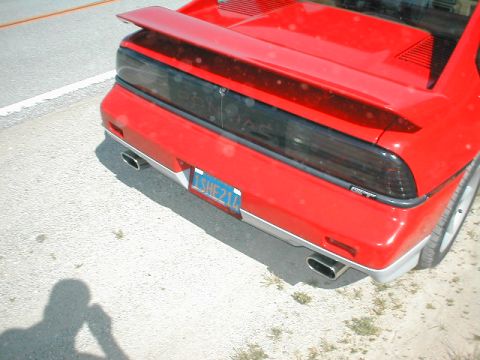 1986 Pontiac Fiero - The rear of a red 1986 Pontiac Fiero is shown, a spoiler and dual exhaust pipes.