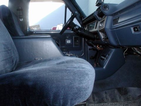 1985 Ford Bronco - Interior of a truck shot from the passenger side across a blue cloth split bench seat toward the dash, steering wheel and floor-mounted shi…