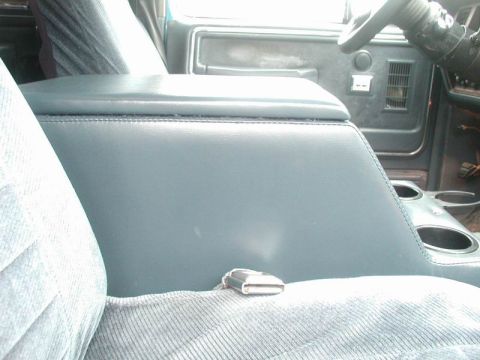 1985 Ford Bronco - Close-up of a finished blue vinyl center console installed between the front seats of a truck, showing the stitched lid, chrome latch and t…
