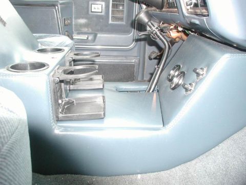 1985 Ford Bronco - Rear view of a blue vinyl center console in a truck with its fold-out dual cup holders extended toward the back seat and additional cup rec…