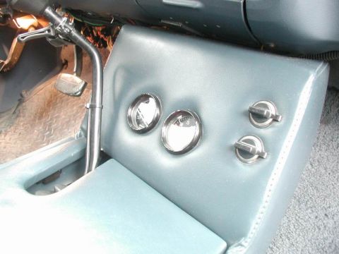 1985 Ford Bronco - Angled close-up of the blue vinyl center console side panel in a truck, with two chrome gauge bezels and two chrome switch knobs set into t…