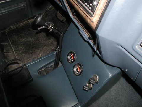 1985 Ford Bronco - Overhead view of the driver side of a custom blue vinyl center console in a truck, with two round gauges and two chrome switches on its ang…
