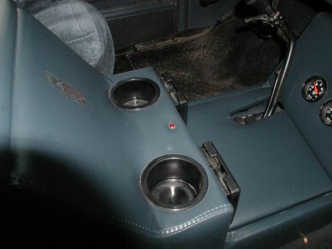1985 Ford Bronco - Top-down detail of a custom blue vinyl center console showing two recessed round cup holders, a small red indicator LED and the folded rear…