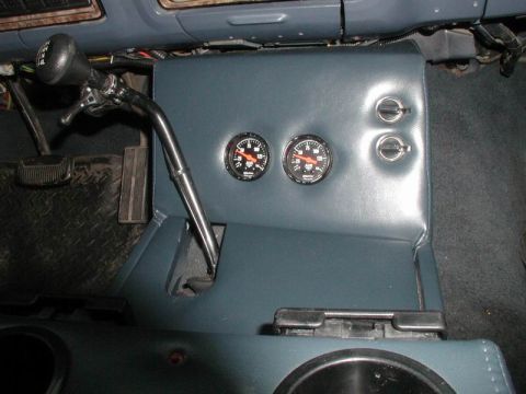 1985 Ford Bronco - Overhead interior shot of a blue vinyl transmission-hump console with two aftermarket Auto Meter round gauges mounted in the vertical face…
