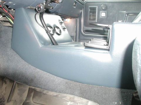 1985 Ford Bronco - Low passenger-side angle along a custom blue vinyl-covered center console showing the smooth stitched side panel, the gauge/switch face wit…