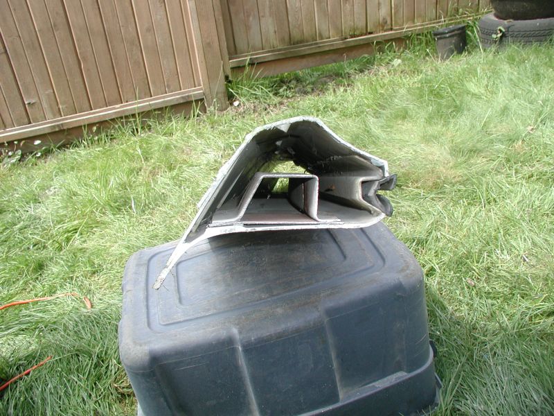 Damaged silver and black metal car part on a black plastic bin