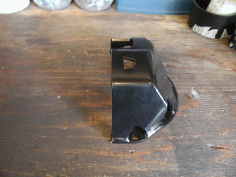 1985 Ford Bronco - A black metal part, possibly a bracket or cover, is shown on a wooden surface. The part has several holes and a cut-out section.