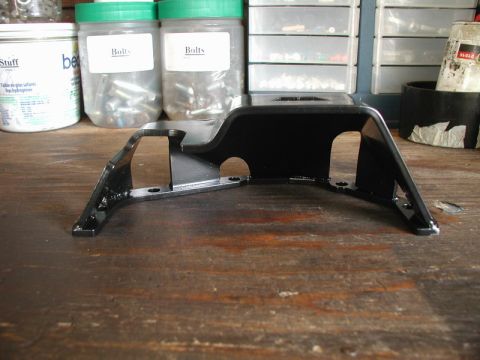 1985 Ford Bronco - A black metal bracket with mounting holes is shown on a wooden workbench. In the background, two clear plastic containers labeled "Bolts" a…