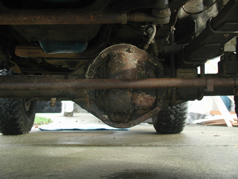 Underside of a vehicle showing a rusty differential, leaf springs, and off-road tires.