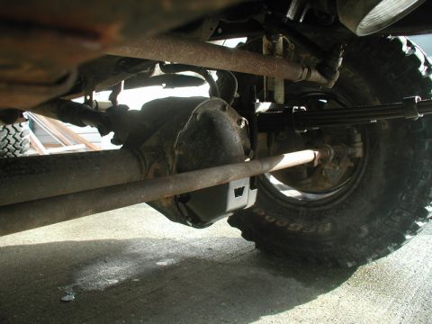 1985 Ford Bronco - The underside of a vehicle, showing the front axle, steering linkage, and a leaf spring assembly with a BFGoodrich tire. The scene appears…