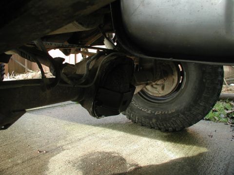 1985 Ford Bronco - The underside of a vehicle's rear axle and differential is shown, with a black skid plate installed over the differential. A tire with "Mud…