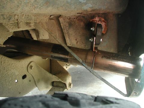 1985 Ford Bronco - Underbody view of a newly installed stainless exhaust tailpipe routed past the rear frame rail and leaf spring, hung from a bolted-on brack…