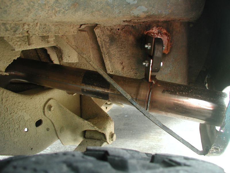 Stainless tailpipe under vehicle hung from bolted bracket on rusty frame