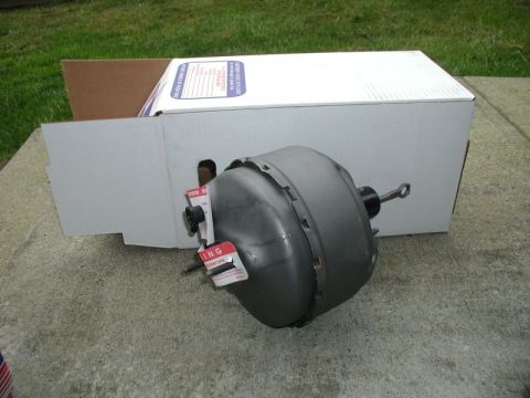 1985 Ford Bronco - A gray brake booster is shown in front of a white cardboard box. Red and white warning labels are attached to the brake booster.