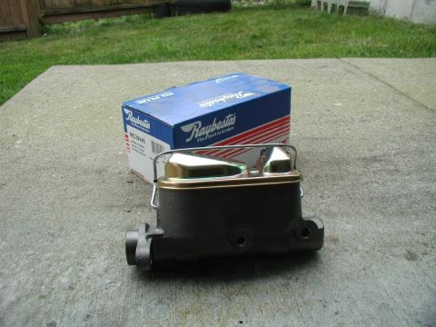 1985 Ford Bronco - A new Raybestos master cylinder is shown in its blue and white box, resting on a concrete surface with grass and a wooden fence in the back…