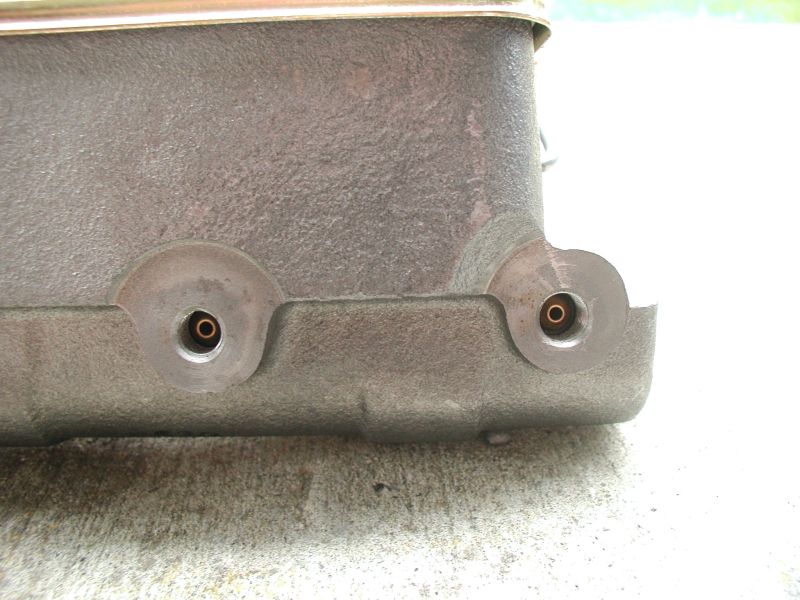 Close-up of cast metal part with two threaded ports and brass fittings.