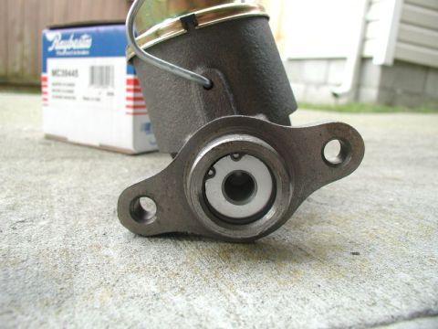 1985 Ford Bronco - A close-up of a master cylinder with a Raybestos box in the background. The master cylinder is made of dark gray metal and has a silver pis…