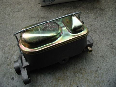 1985 Ford Bronco - A new, dark gray master cylinder with a gold-colored lid is shown resting on a concrete surface. The lid has embossed text that is partiall…