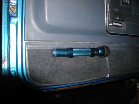 1985 Ford Bronco - A blue flashlight is mounted with black clips to the interior door panel of a vehicle. The panel has a textured gray fabric insert and a bl…