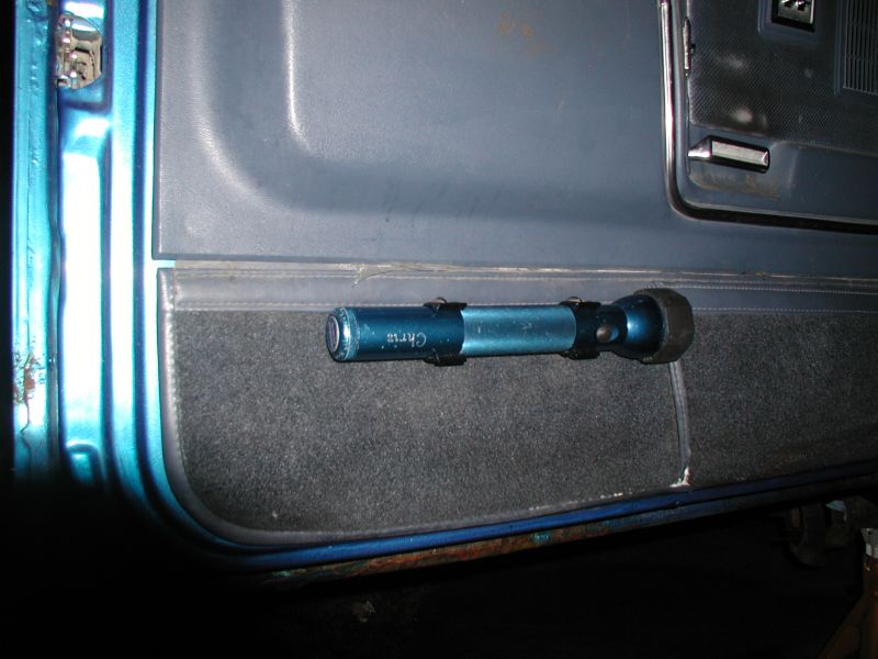 Blue flashlight mounted on the interior door panel of a vehicle.