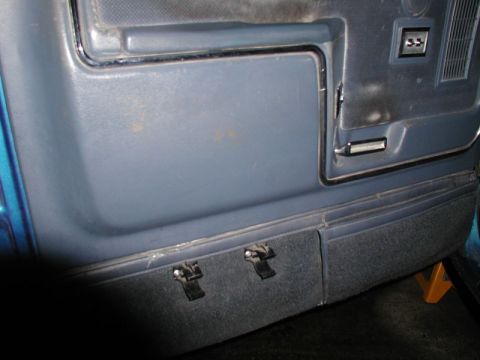 1985 Ford Bronco - The interior door panel of a blue vehicle shows a large gray section with a chrome trim outline. Below this, a darker gray carpeted section…