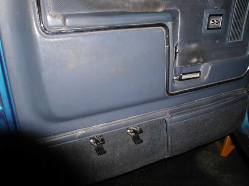 Interior door panel of a blue vehicle with gray panel and carpeted lower section with clips.